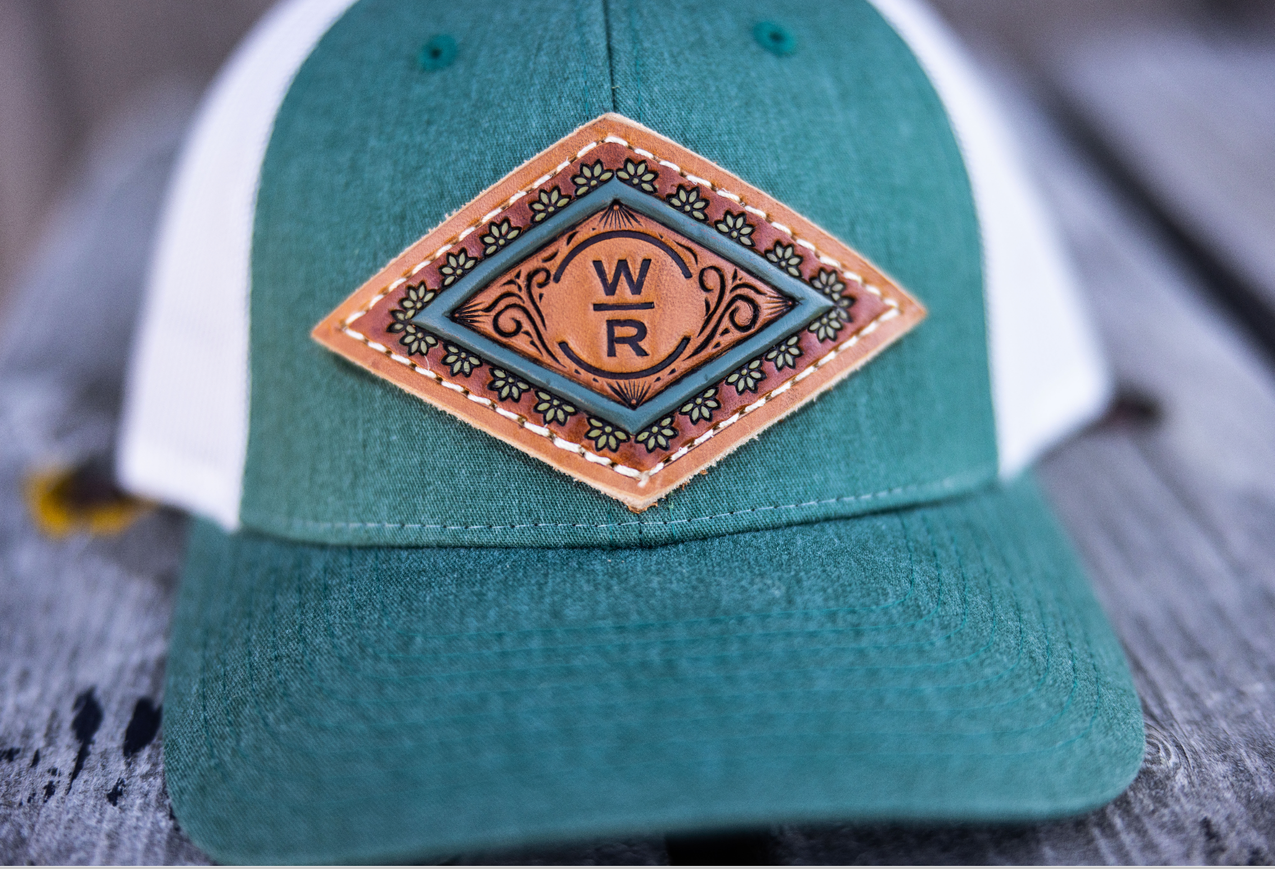 Teal and white cap with a leather patch featuring a logo on a wooden surface