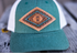 Teal and white cap with a leather patch featuring a logo on a wooden surface